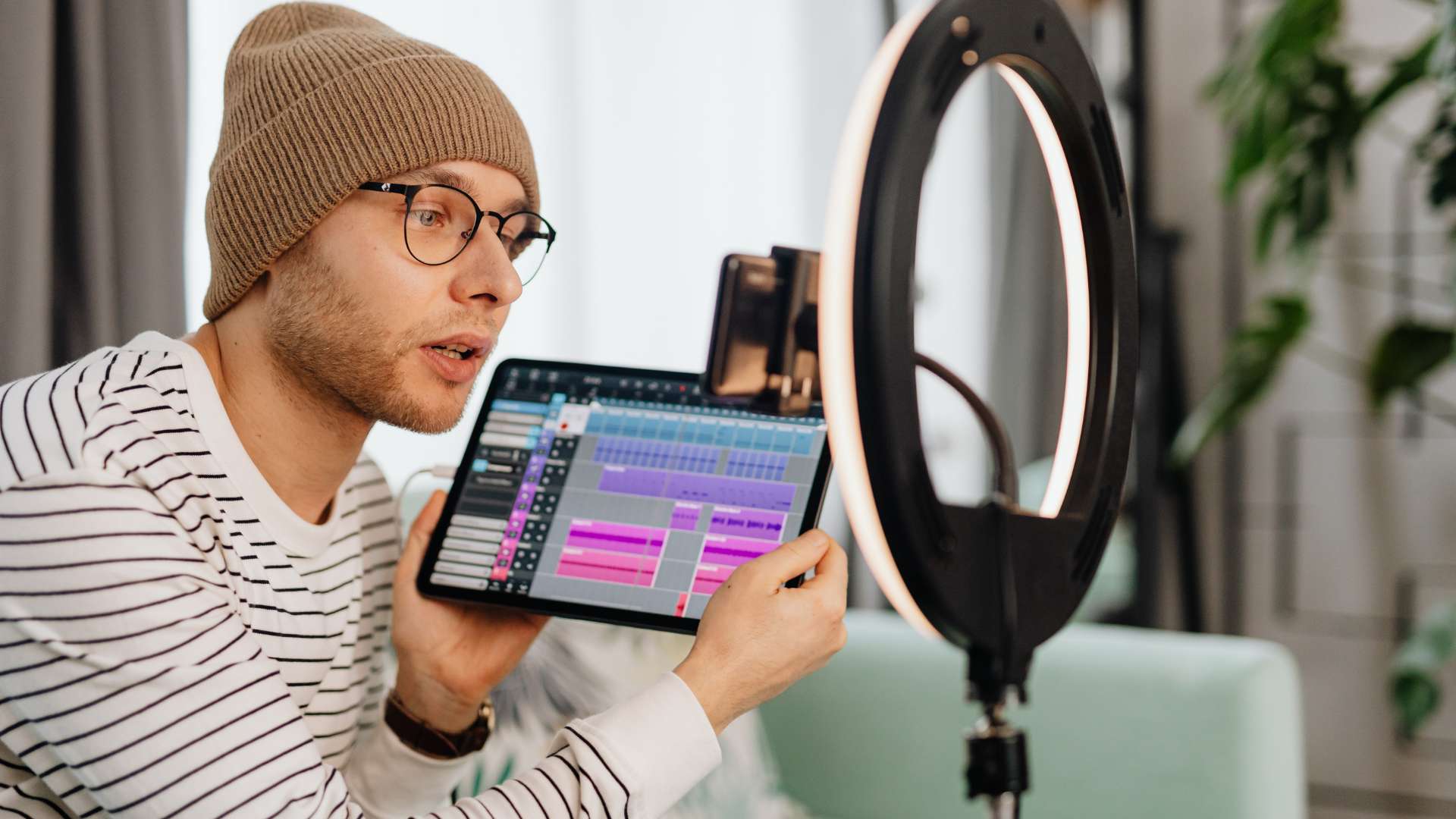 Un ragazzo, con un tablet in mano, mostra un programma di video editing a una camera illuminata da una ring light