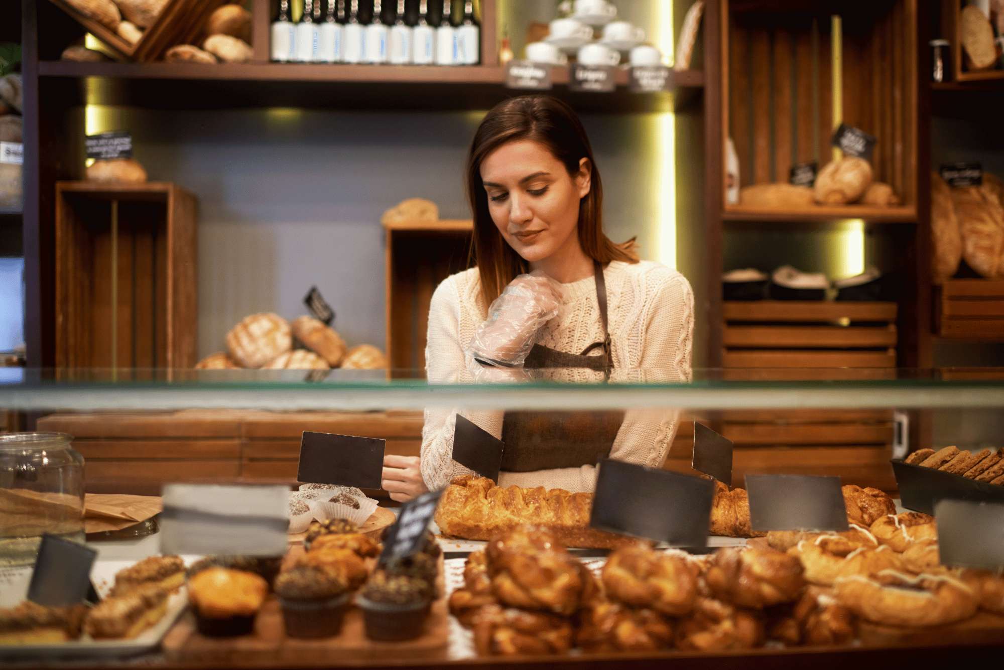 Una ragazza col grembiule dietro il bancone di una bakery piena di brioche